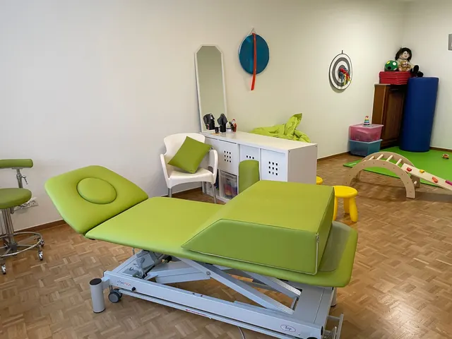 Behandlungsraum mit grüner Therapieliege und Spielbereich für Kinder